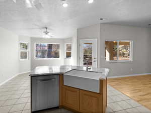 Kitchen with a kitchen island with sink, stainless steel dishwasher, sink, and light tile patterned floors