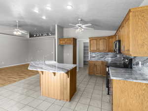 Kitchen featuring light stone counters, light tile patterned floors, tasteful backsplash, a breakfast bar area, and range with electric cooktop