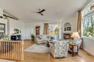 Living room featuring lofted ceiling, a fireplace, ceiling fan, and light hardwood / wood-style floors