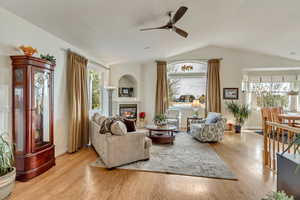 Living room with lofted ceiling, a fireplace, ceiling fan, and light wood-type flooring