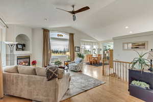 Living room with vaulted ceiling, a fireplace, ceiling fan, and light hardwood / wood-style flooring