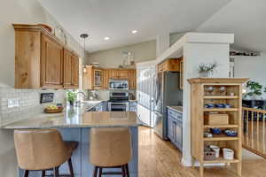 Kitchen with appliances with stainless steel finishes, kitchen peninsula, vaulted ceiling, and tasteful backsplash