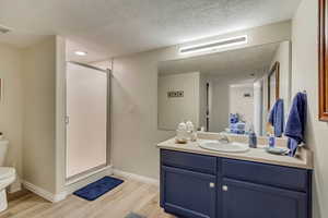 Bathroom featuring toilet, a textured ceiling, a shower with shower door, wood-type flooring, and vanity