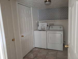 Washroom with a textured ceiling, light tile patterned floors, and independent washer and dryer