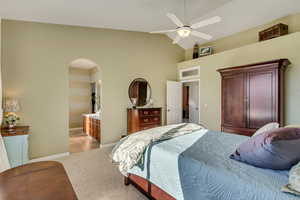 Carpeted bedroom with lofted ceiling, ensuite bathroom, and ceiling fan