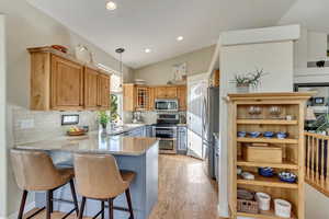 Kitchen featuring kitchen peninsula, stainless steel appliances, a kitchen bar, lofted ceiling, and backsplash