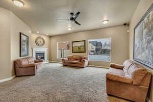 Living room with a tiled fireplace, ceiling fan, and carpet flooring