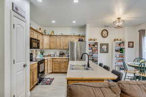 Kitchen with decorative light fixtures, a notable chandelier, black appliances, light hardwood / wood-style floors, and sink