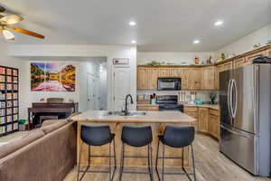 Kitchen featuring a kitchen breakfast bar, a kitchen island with sink, black appliances, sink, and light hardwood / wood-style flooring