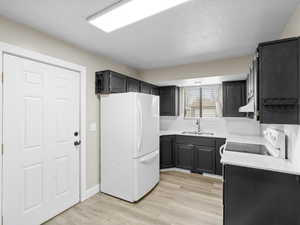 Kitchen featuring electric range, white refrigerator, light  wood-style floors, and sink