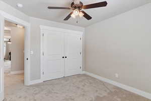 Unfurnished bedroom featuring ceiling fan, light colored carpet, and a closet