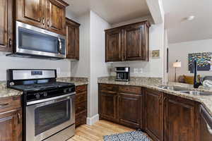 Kitchen featuring sink, light hardwood / wood-style floors, dark brown cabinets, light stone countertops, and appliances with stainless steel finishes