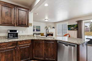 Kitchen featuring kitchen peninsula, dishwasher, dark brown cabinets, and sink