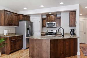 Kitchen featuring sink, light hardwood / wood-style floors, dark brown cabinets, light stone countertops, and appliances with stainless steel finishes