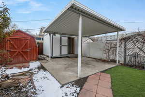 Snow covered patio with a lawn and a storage shed