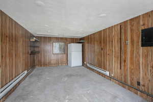 Unfurnished room with concrete floors, a baseboard radiator, and wood walls