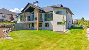 Back of property with a balcony, stucco siding, a yard, and a chimney