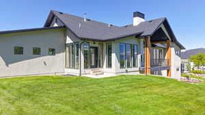 Rear view of property with stucco siding, a lawn, a shingled roof, and a chimney