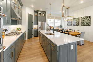 Kitchen with hanging light fixtures, a 10' center island with sink, wood-style floors, appliances with stainless steel finishes, and sink. Photo of Finland Model Home not subject property