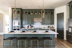 Kitchen featuring an island with sink, exhaust hood, wood-type flooring, and pendant lighting. Photo of Finland Model Home not subject property