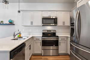 Kitchen featuring stainless steel appliances, sink, pendant lighting, light hardwood / wood-style flooring, and white cabinetry