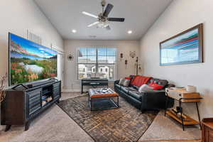 Carpeted living room featuring ceiling fan and vaulted ceiling