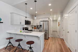 Kitchen featuring white cabinets, appliances with stainless steel finishes, kitchen peninsula, and pendant lighting