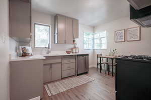 Kitchen with gray cabinetry, light hardwood / wood-style floors, black range with gas stovetop, sink, and stainless steel dishwasher