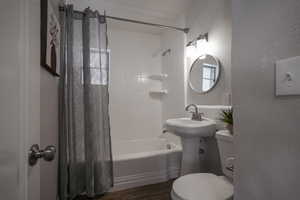 Bathroom featuring wood-type flooring, shower / bathtub combination with curtain, and toilet