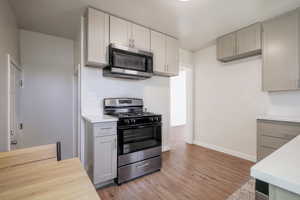 Kitchen with appliances with stainless steel finishes, light hardwood / wood-style floors, and gray cabinets