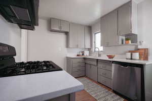 Kitchen featuring dishwasher, gray cabinets, light hardwood / wood-style floors, gas stove, and ventilation hood