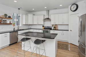Kitchen featuring sink, white cabinets, wall chimney range hood, and appliances with stainless steel finishes