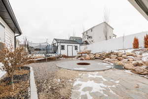 View of patio with an outdoor fire pit, a trampoline, and a storage shed