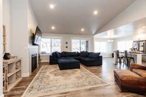 Living room with a tiled fireplace, a notable chandelier, hardwood / wood-style floors, and vaulted ceiling