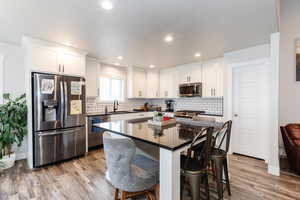 Kitchen with a breakfast bar, a kitchen island, light wood-type flooring, white cabinetry, and appliances with stainless steel finishes