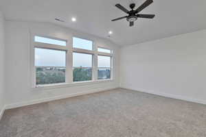 Carpeted spare room with ceiling fan and vaulted ceiling