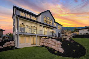 Back house at dusk with a mountain view, a yard, a balcony, and central AC unit