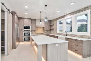 Kitchen with stainless steel appliances, a barn door, light stone countertops, a kitchen island, and pendant lighting