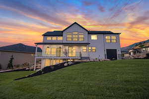 Back house at dusk featuring a garage and a lawn