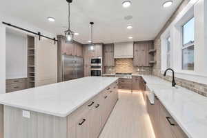 Kitchen with built in appliances, light stone countertops, pendant lighting, a large island, and a barn door