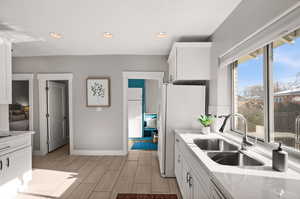 Kitchen with white cabinetry, sink, light stone countertops, and white refrigerator