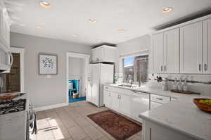 Kitchen featuring decorative backsplash, light stone countertops, white appliances, sink, and white cabinets