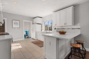 Kitchen with white appliances, backsplash, white cabinets, kitchen peninsula, and a breakfast bar area