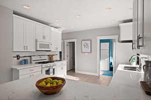 Kitchen with white cabinetry, sink, light stone countertops, backsplash, and white appliances