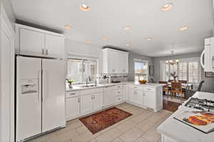 Kitchen featuring kitchen peninsula, white appliances, white cabinets, and sink