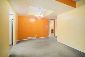 Spare room with a textured ceiling, a raised ceiling, a chandelier, and carpet flooring