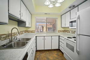 Kitchen featuring sink, white cabinetry, white appliances, a raised ceiling, and backsplash