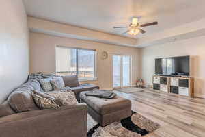 Living room with ceiling fan, light hardwood / wood-style flooring, and a tray ceiling