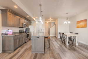 Kitchen featuring decorative light fixtures, a center island with sink, a breakfast bar, stone countertops, and appliances with stainless steel finishes