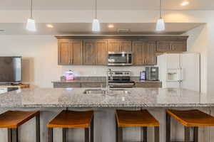 Kitchen with stainless steel appliances, decorative light fixtures, sink, and light stone countertops